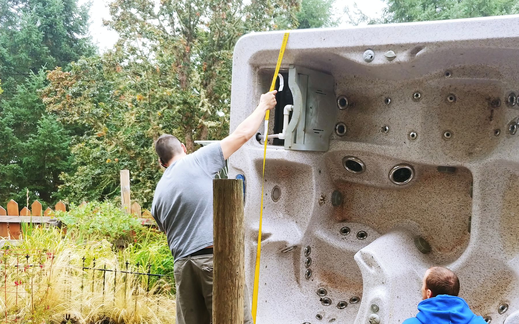 Confidence movers strapping a hot tub standing on its side in a narrow side yard